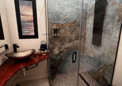 The shower has a full panel system with rainfall waterfall shower head, and massage body jets. Artisnal floor base made with locally sourced pebbles and marbled ocean coloured wall tiles.