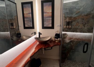 Bronze glass basin with naturally cut polished wood vanity shelf in bathroom, and folded towels.