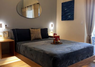 Side view of floating queen bed with complimentary rum punch with flower arrangement with backlit mirror above.