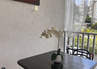 Verandah view over neighbourhood including two-seater breakfast table with a white orchid. Seascape of a surf barrel wave framing a sunset on the wall.