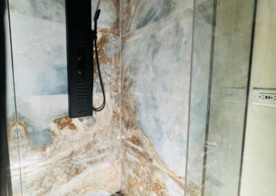 The shower has a full panel system with rainfall waterfall shower head, and massage body jets. Artisnal floor base made with locally sourced pebbles and marbled ocean coloured wall tiles.