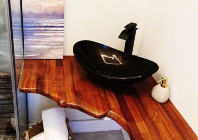 Naturally cut polished wood vanity shelf in bathroom, with bronzed glass sink and seascape artwork.