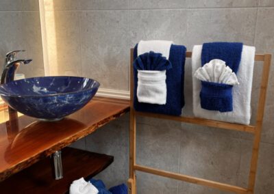 Blue glass basin with naturally cut polished wood vanity shelf in bathroom, and folded towels.