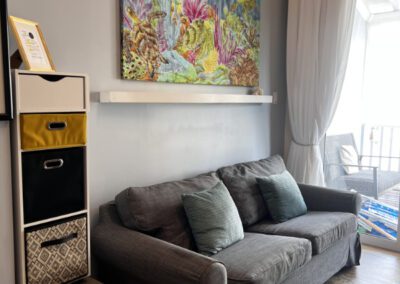 Three seater sofa bed in living area with shelves and colourful batik painting on wall.