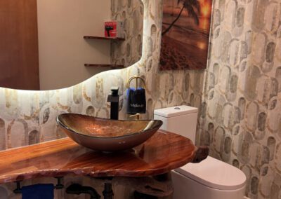 Naturally cut polished wood vanity shelf in bathroom, with bronzed glass sink and seascape artwork.