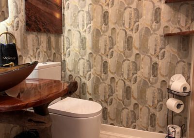 Naturally cut polished wood vanity shelf in bathroom, with bronzed glass sink and seascape artwork.