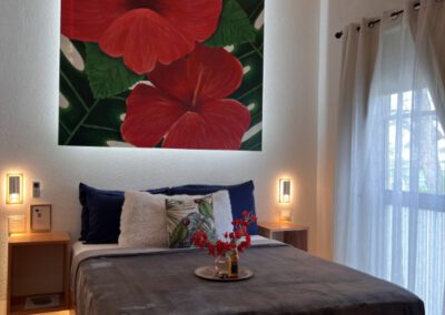 Large Hibiscus painting hangs over queen bed with bougainvillea flowers.