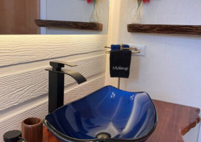 Blue polished glass basin on naturally cut polished wood vanity shelf in bathroom, with wooden carved toiletry holders.