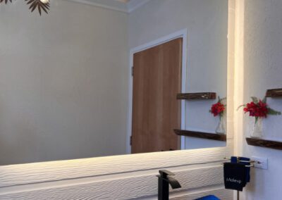 Blue polished glass basin on naturally cut polished wood vanity shelf in bathroom, with view of locally designed artisnal light fitting in mirror.