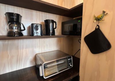 Kitchen counter and shelves showing toaster oven, sink, crockery, kettle, coffee maker and toaster.