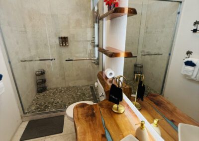 Glass door shower unit with artisnal floor base made with locally sourced pebbles and neutral coloured wall tiles.