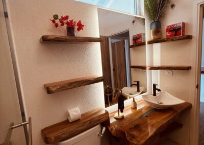 Naturally cut polished wood vanity shelf in bathroom, with white ceramic sink and hairdryer.