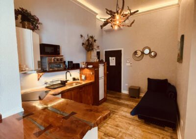 Kitchen showing breakfast bar spanning into the living room. Microwave, toaster oven, hob, fridge, with crockery and complimentary tea / coffee. Futon nestled in hallway corner.