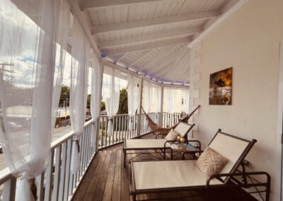 Verandah with two long sun loungers, with side table and two golden wine goblets, with hammock in the background.
